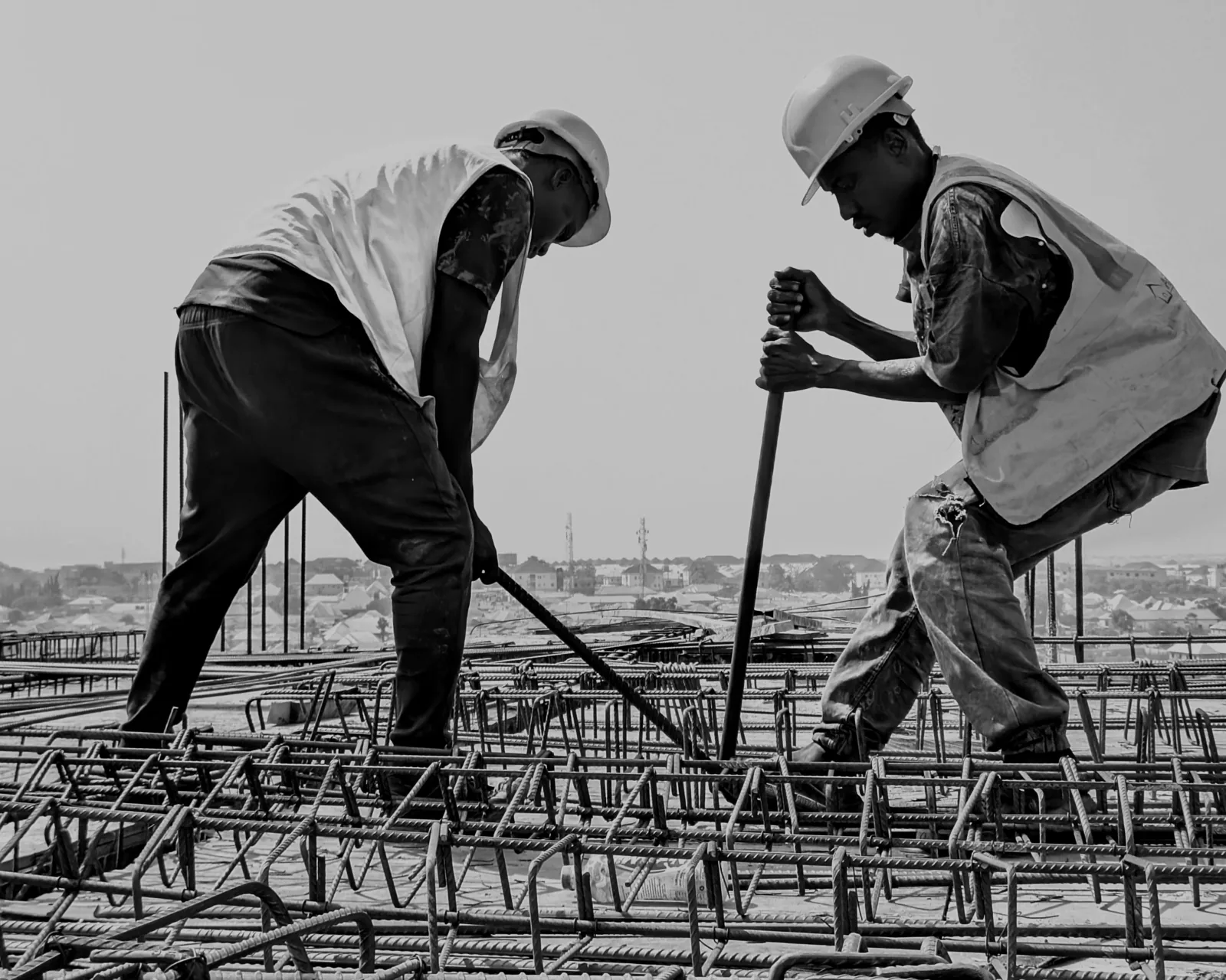 Ironworkers tying rebar on a deck with a city skyline behind
