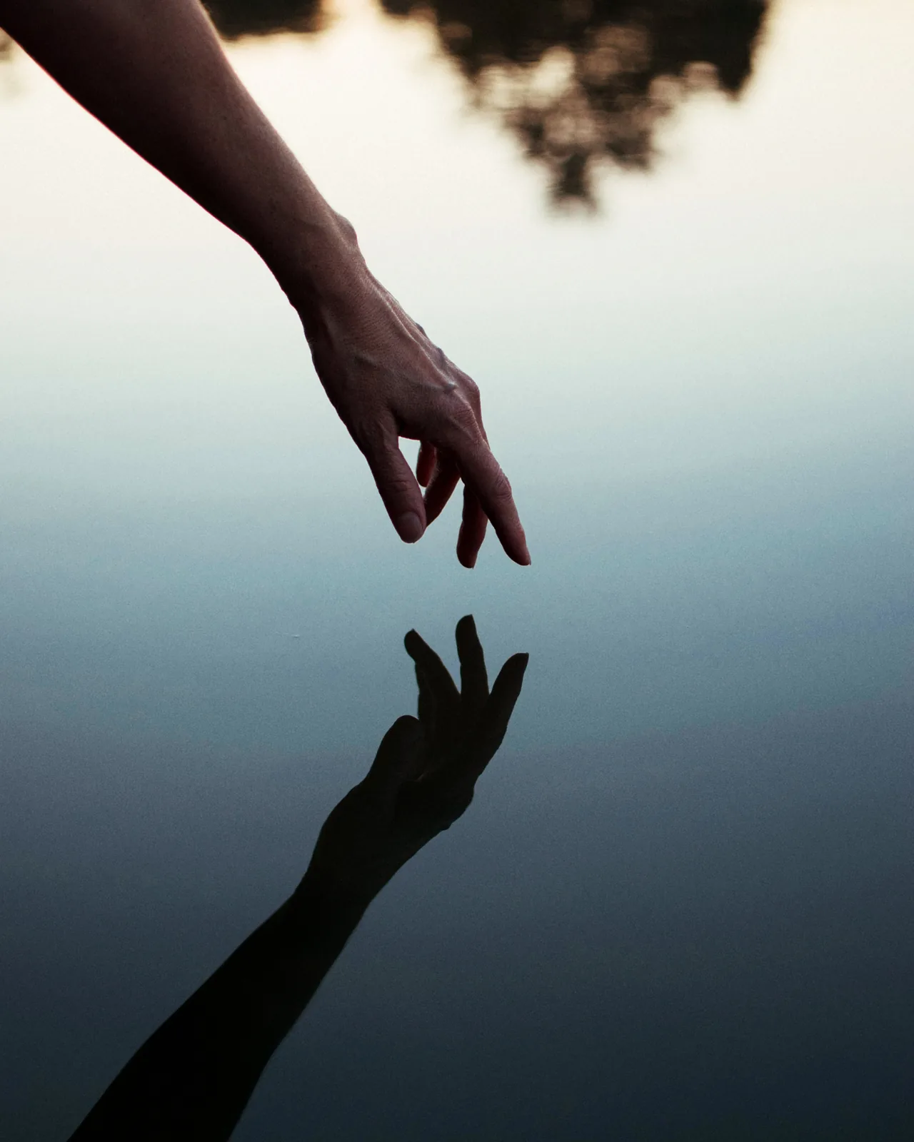 A hand touching its reflection at a still water surface